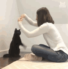 a woman playing with a black cat with a picture of a cat on the wall behind her a woman playing with a black cat with a picture of a cat on the wall behind her