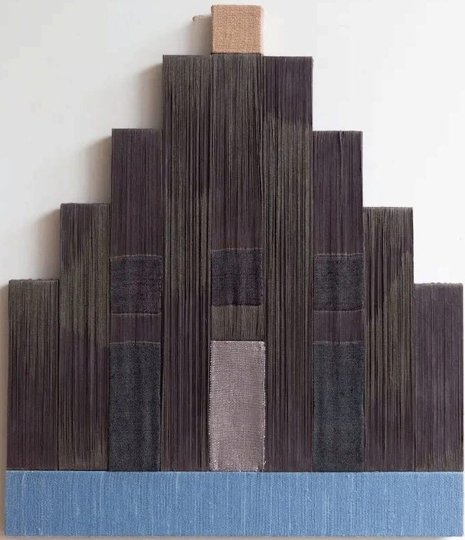 Carolina Jiménez, Glimmer, 2026. A stepped, pyramid-shaped weaving in dense dark brown and charcoal thread, with a narrow vertical strip of pale mauve at the center, a small natural block at the top, and a band of soft blue across the bottom. Carolina Jiménez, Glimmer, 2026. A stepped, pyramid-shaped weaving in dense dark brown and charcoal thread, with a narrow vertical strip of pale mauve at the center, a small natural block at the top, and a band of soft blue across the bottom.