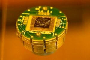 Chalmers researchers have developed tiny memory devices using a novel, atomically thin material, visible as clusters of golden dots on the chip surface. The material combines two opposing magnetic forces, generating an exchange force and a tilted overall magnetic alignment. This unusual coexistence could simplify device fabrication while reducing energy use in memory devices by a factor of ten, offering major benefits for future computers, artificial intelligence, and advanced data processing.