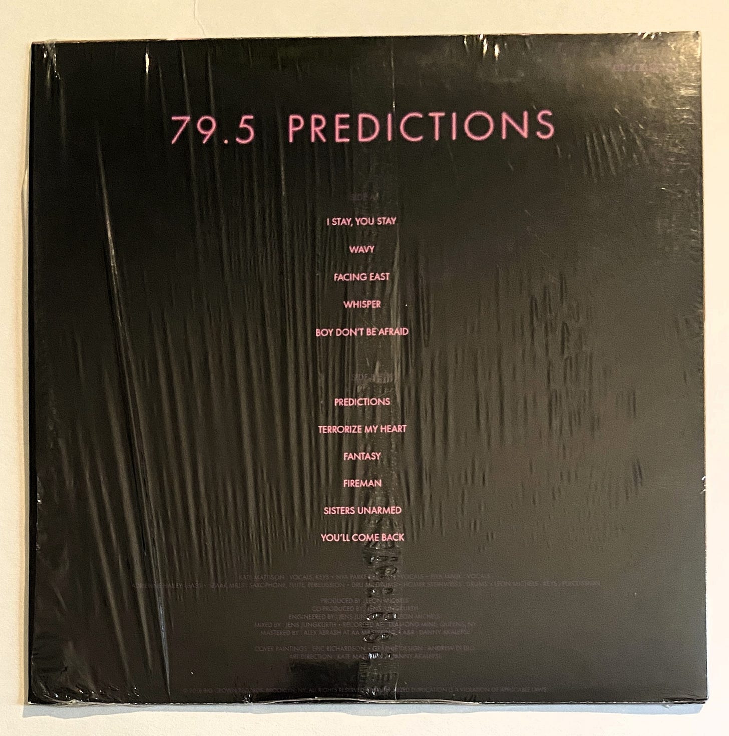 the back cover of 79.5's Predictions still in the shrink wrap. the band name, album title, and song titles appear in pink neon text with the credits in purple text on a black background. the back cover of 79.5's Predictions still in the shrink wrap. the band name, album title, and song titles appear in pink neon text with the credits in purple text on a black background.
