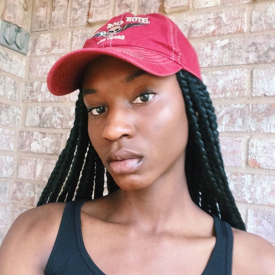 a selife of me in a red cap that reads Hard Rock Hotel Las Vegas with a skull that has wings on either side of it. I am in a black tank top and showcasing 3/4 of my face.