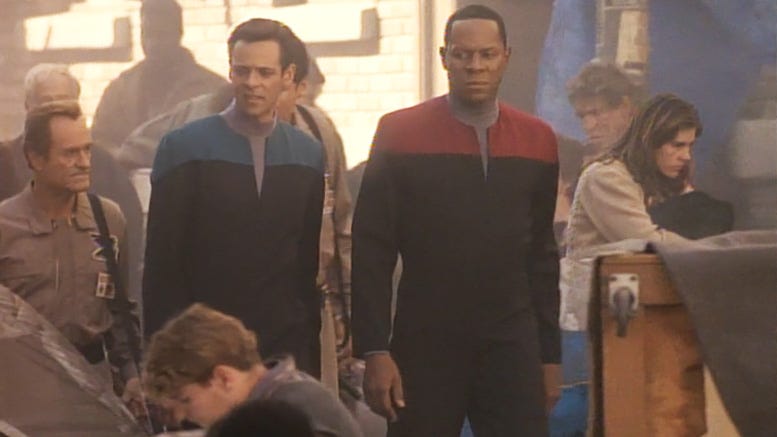 Two Star Trek officers wander through a concentration camp in 2024 Los Angeles, from a time travel episode in DS9. The Federation officers are grim-faced at all the signs of suffering.