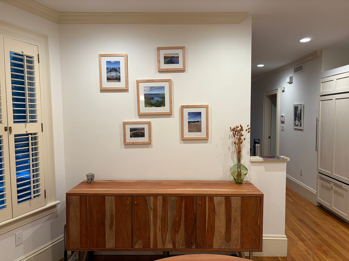 Dining room before the art update, with five small framed landscape prints arranged above a wood sideboard near a bay window.