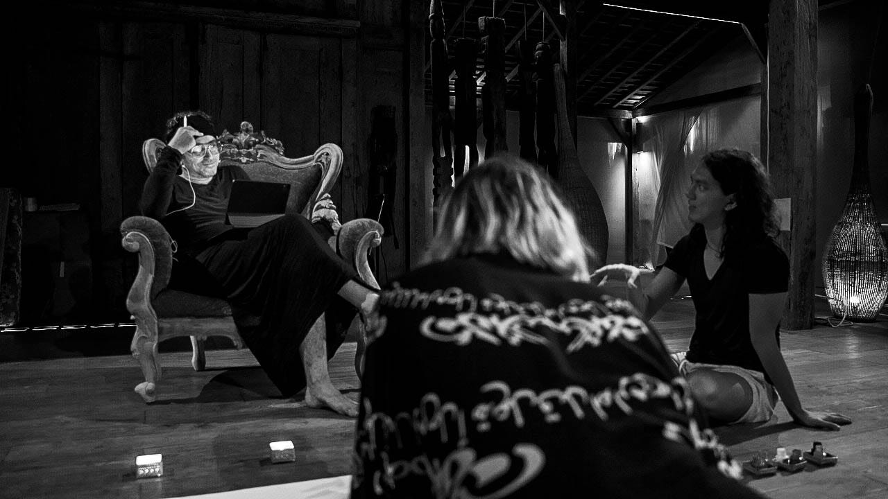 Black and white photo of Michael Perin Wogenburg sitting on a vintage armchair in a yoga shala in Bali, with two participants listening in the foreground