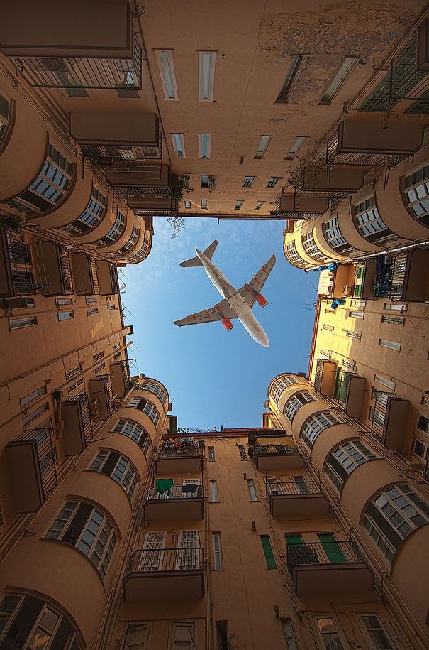 This may contain: an airplane is flying high in the sky between two buildings, looking up at it