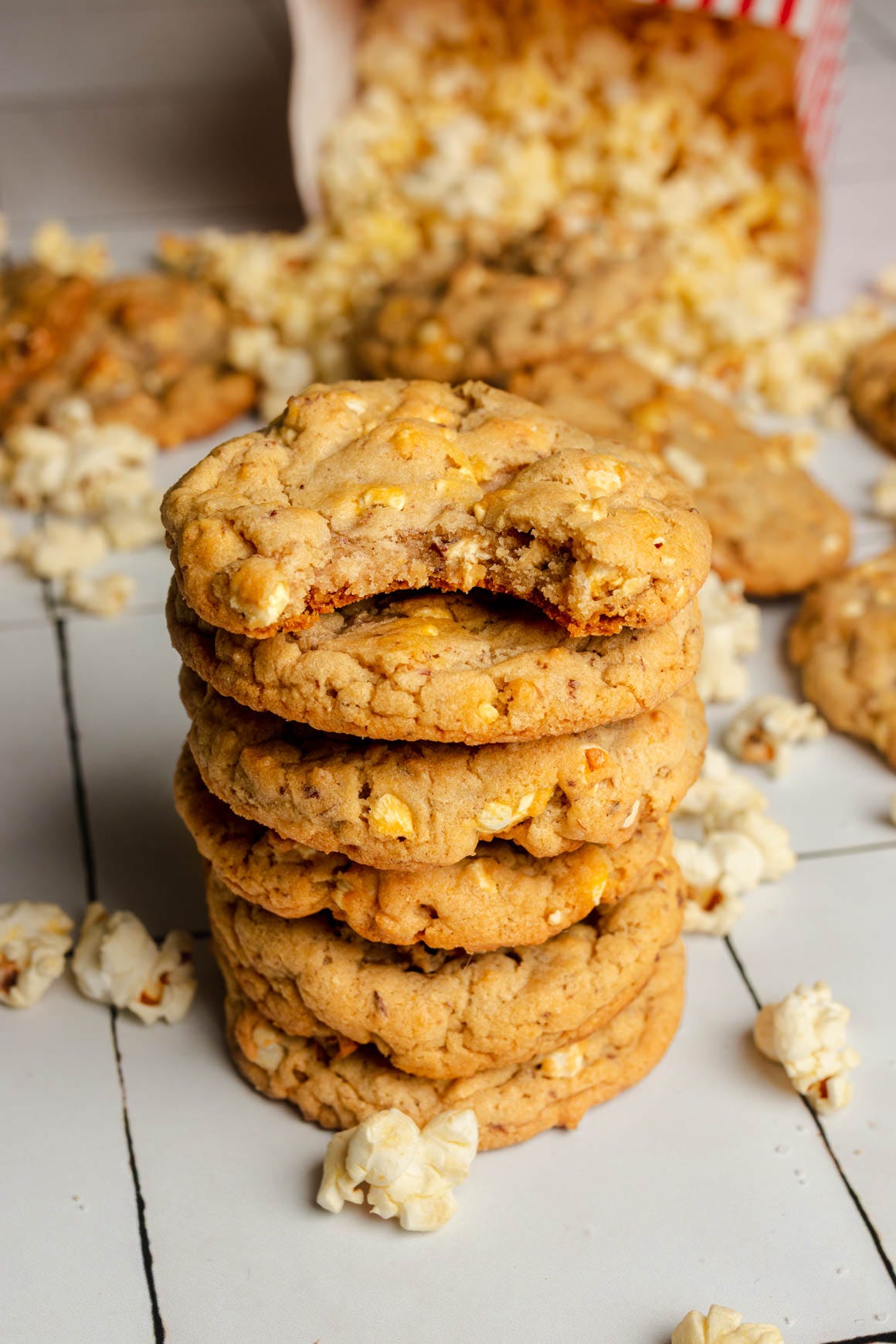 Stack of cookies, with the top one that has a bite out of it. A bag of popcorn is spilling out in the background.