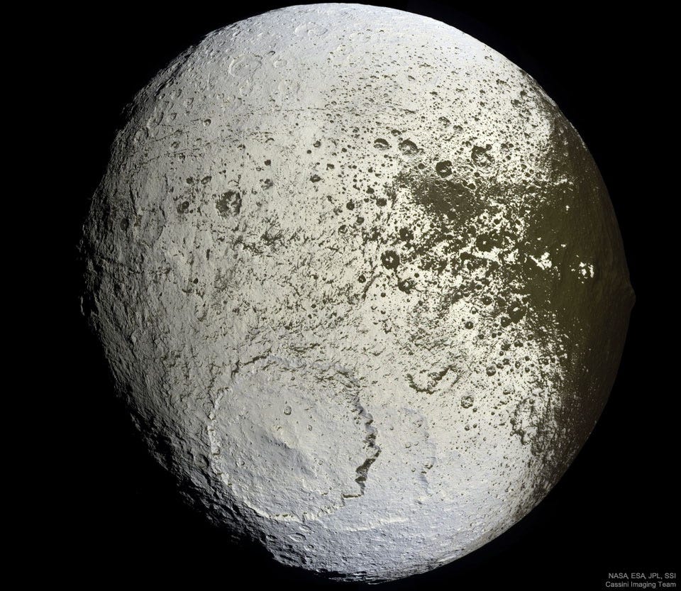 An unusually colored ball is shown against a
dark background. The ball has numerous craters but
a very large cratered near the lower center. Much of
the ball is light colored, but around the right and
top it is green-brown, with a border area that seems
splattered.
Please see the explanation for more detailed information. An unusually colored ball is shown against a
dark background. The ball has numerous craters but
a very large cratered near the lower center. Much of
the ball is light colored, but around the right and
top it is green-brown, with a border area that seems
splattered.
Please see the explanation for more detailed information.