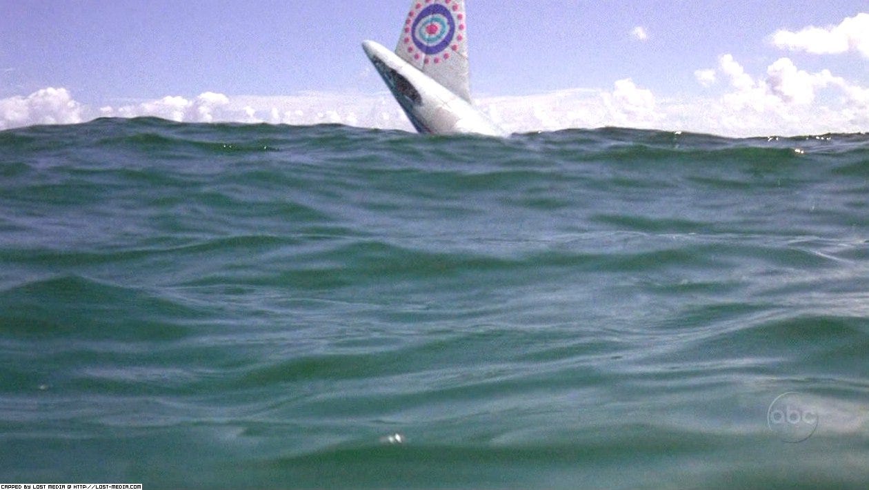 The screen is dominated by ocean waves, with a blue sky adorned with clouds hugging the top of the frame. The tail of Oceanic 815, also seen at the top of the frame, sinks below the waves.