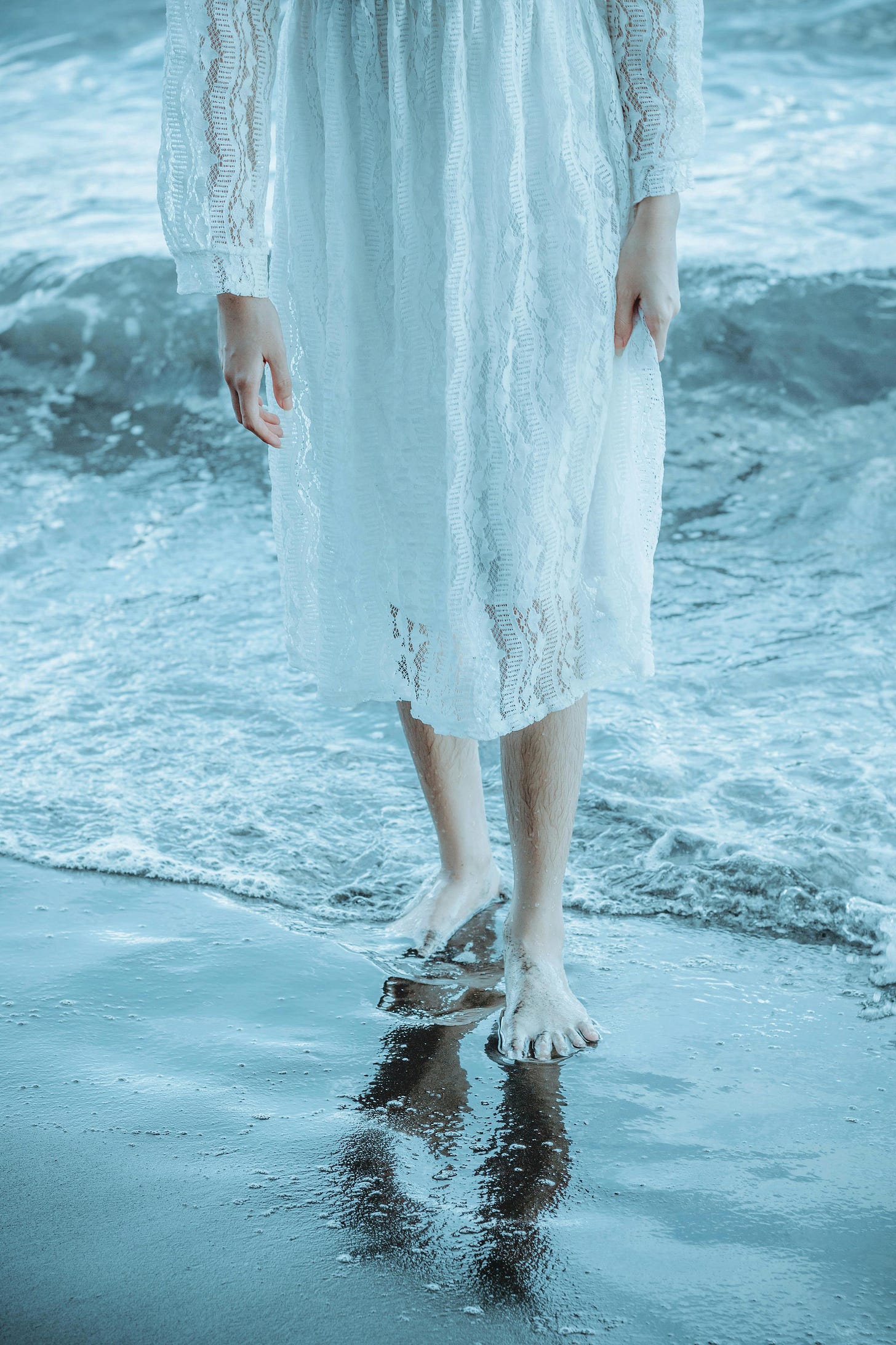 Free A woman in a white dress walks barefoot along the tranquil shore, reflecting elegance and calm. Stock Photo