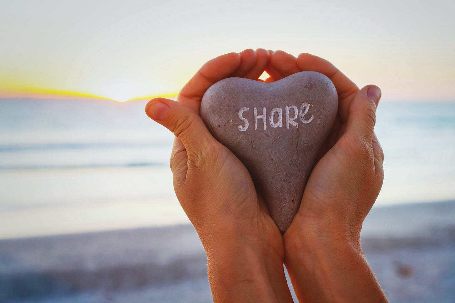 Hands holding a heart shaped rock with the word share etched into it. Adobe Stock Photo. Hands holding a heart shaped rock with the word share etched into it. Adobe Stock Photo.