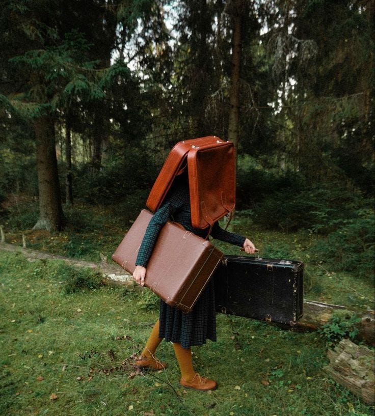 This may contain: a woman carrying two suitcases in the woods