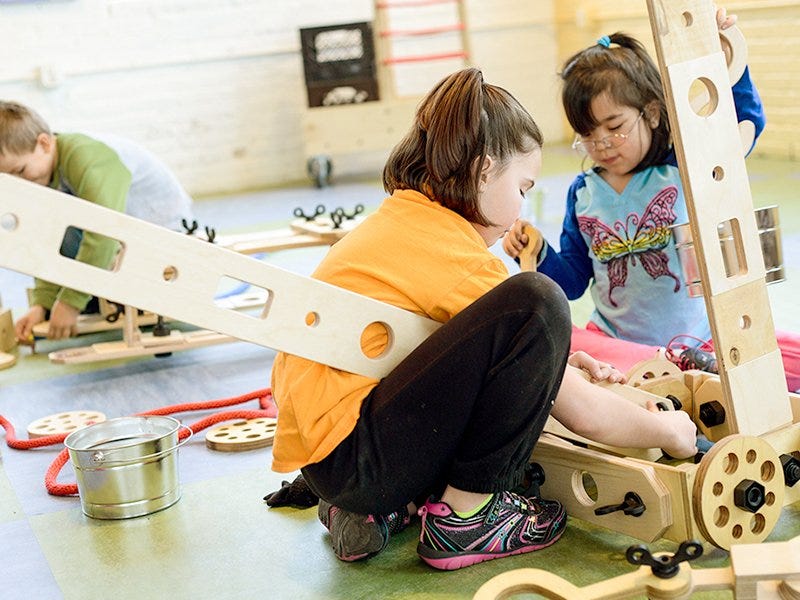 Three children construct a kid-scale structure with Rigamajig parts. Three children construct a kid-scale structure with Rigamajig parts.