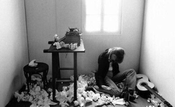 This may contain: a person sitting on the floor with a guitar in front of a pile of paper