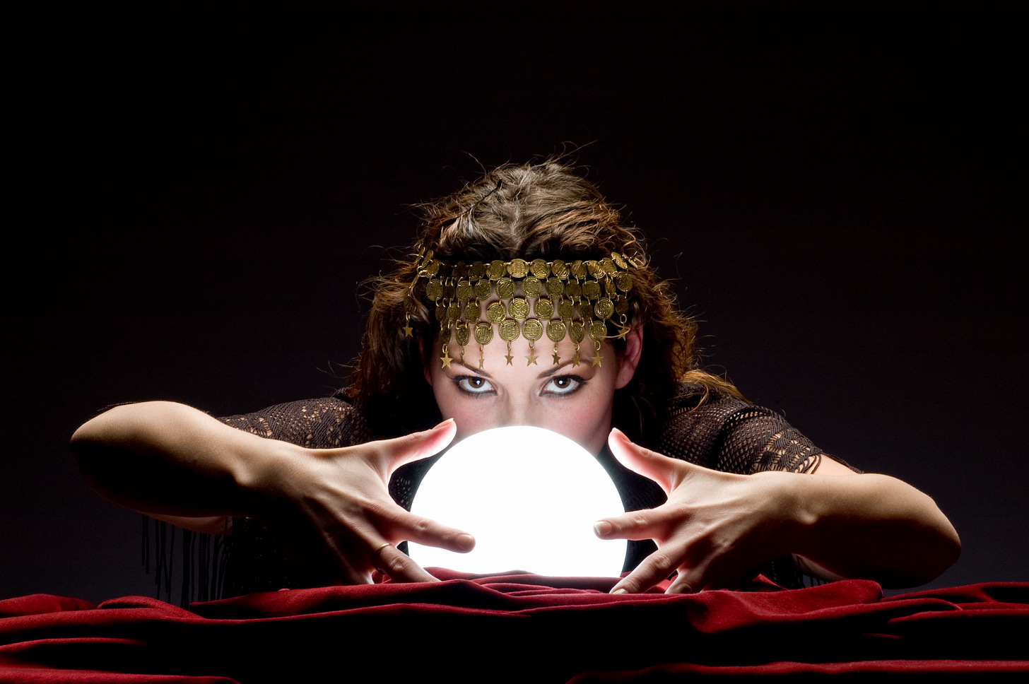 Mysterious focused fortune telling woman wearing a copper hair dress with her hands on a glowing crystal ball looking at the camera Mysterious focused fortune telling woman wearing a copper hair dress with her hands on a glowing crystal ball looking at the camera