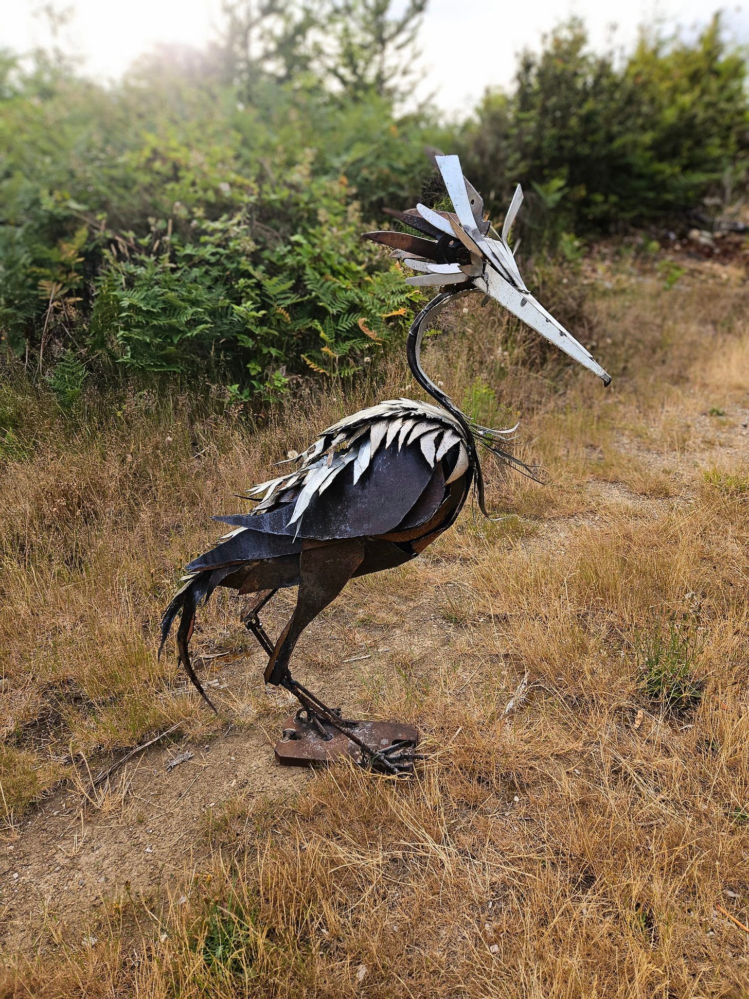 A photo of a large scrap metal sculpture of a expressive and inquisitive looking heron, it's probably 4 ft tall.