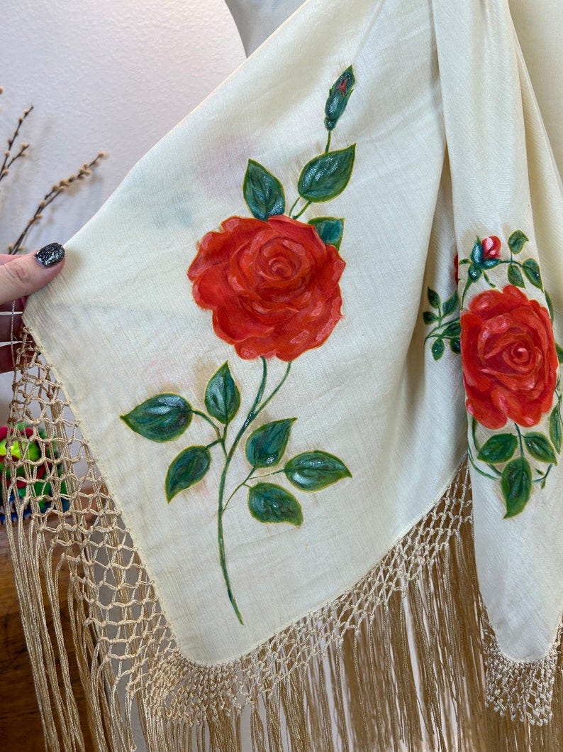 May include: A white shawl with a hand-painted red rose design and a gold fringe border.
