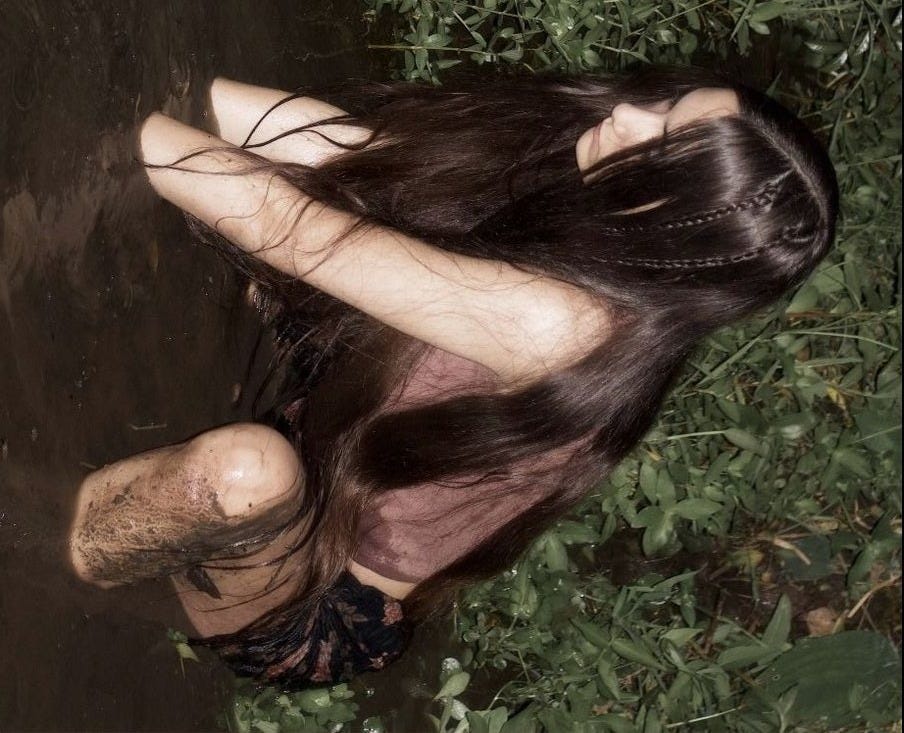 This may contain: a woman is kneeling in the water with her head down and long hair flowing over her body