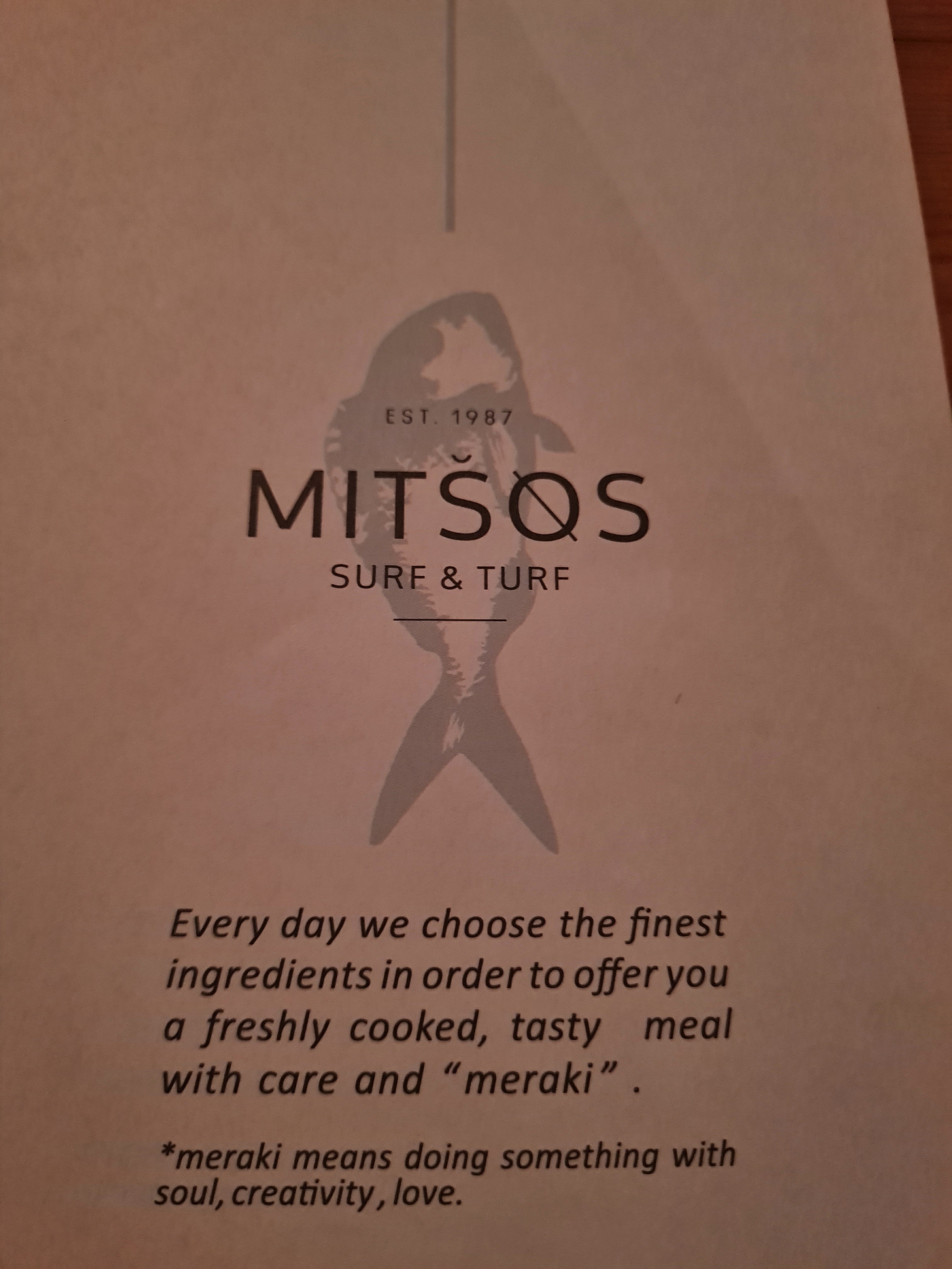 The front of the menu of Mitsos Surf and Turf restaurant in Crete. the copy reads "Every Day we choose the finest ingredients in order to offer you a freshly cooked, tasty meal with care and "meraki". Meraki means doing something with soul, creativity and love.