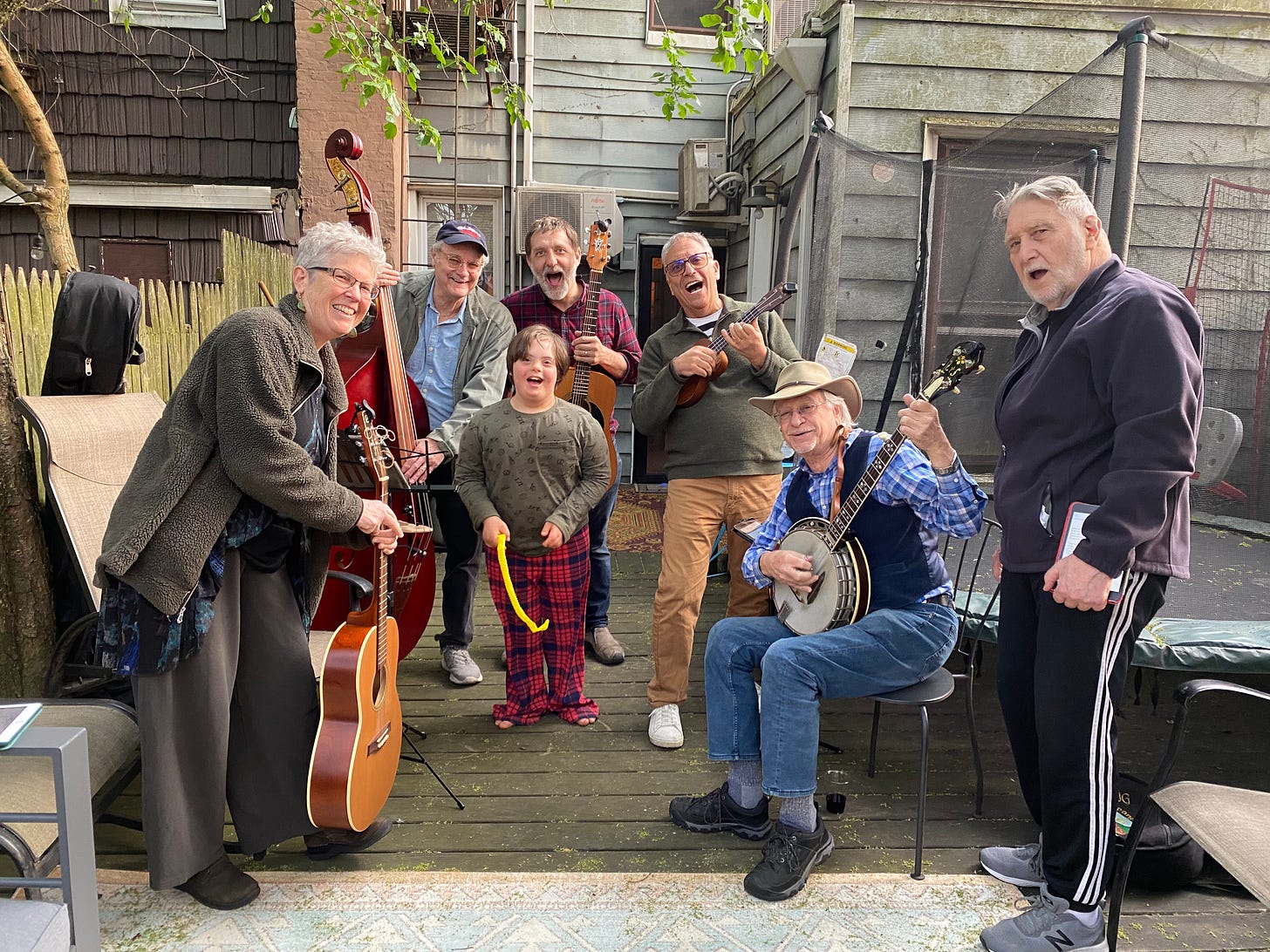 A group of White people of many ages, smiling together, holding musical instruments, standing in a semi-circle outdoors. A group of White people of many ages, smiling together, holding musical instruments, standing in a semi-circle outdoors.