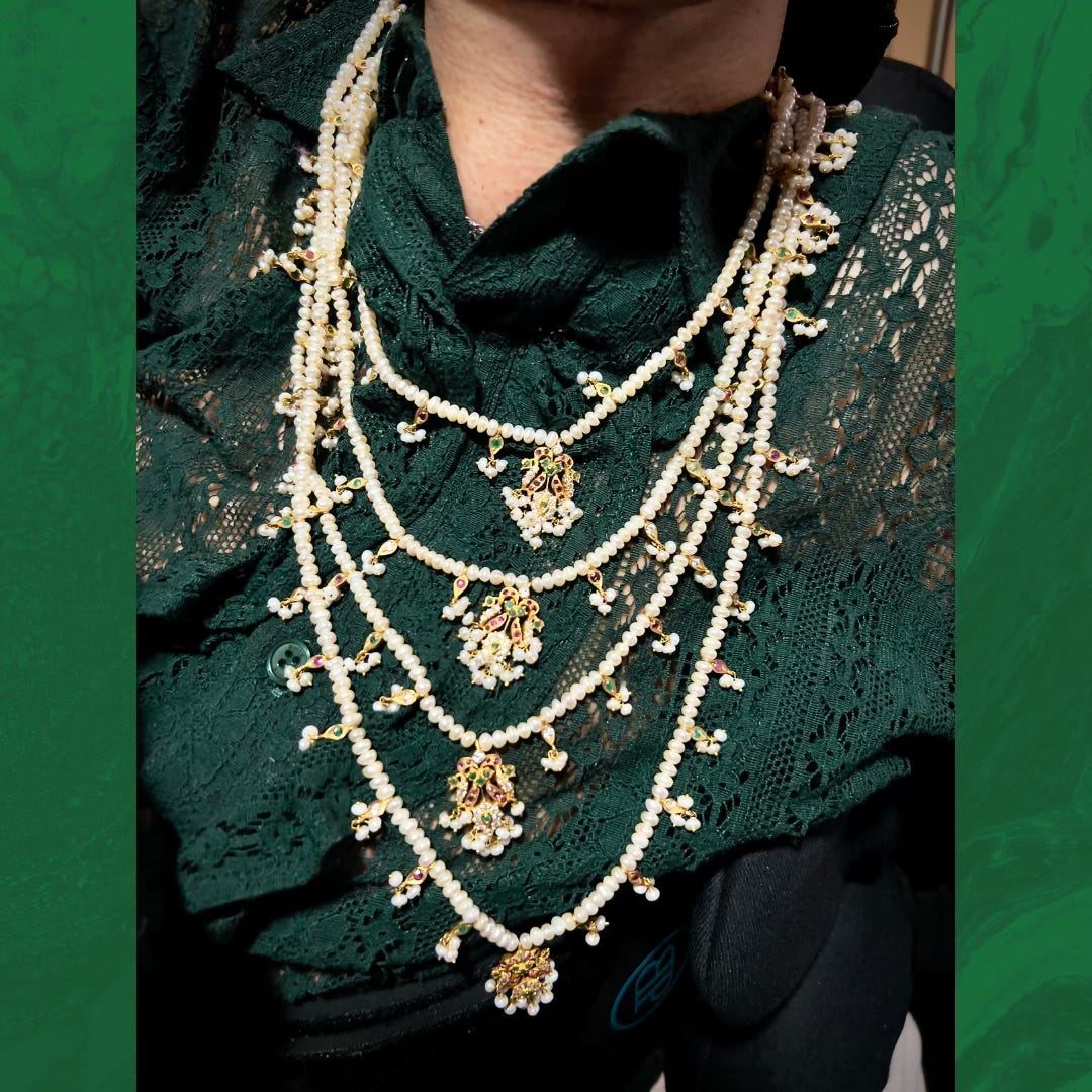 Close-up photo of the four-layered pearl and gemstone necklace Sulaiman is wearing against Sulaiman's green, ruffled lace shirt. Close-up photo of the four-layered pearl and gemstone necklace Sulaiman is wearing against Sulaiman's green, ruffled lace shirt.