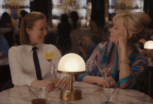 two women sitting at a table with a martini and a lamp two women sitting at a table with a martini and a lamp