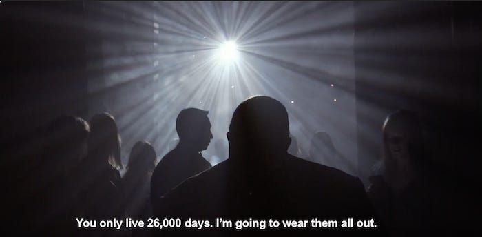 A screenshot from the documentary Quincy of a bright spotlight with Quincy Jones’ silhouette from behind with a caption that says “You only live 26,000 days. I’m going to wear them all out.”