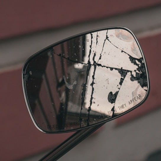 a side view mirror on a motorcycle with a brick building in the background