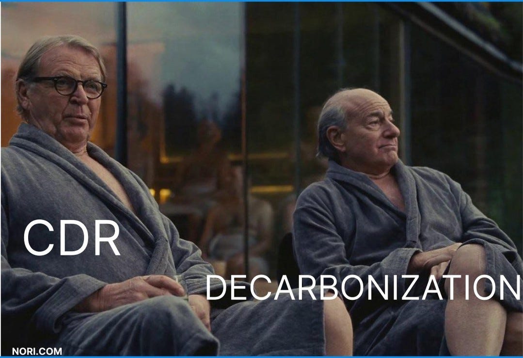 Two older men in grey bathrobes sit side by side looking out a window. One is labelled "CDR", the other "DECARBONIZATION".