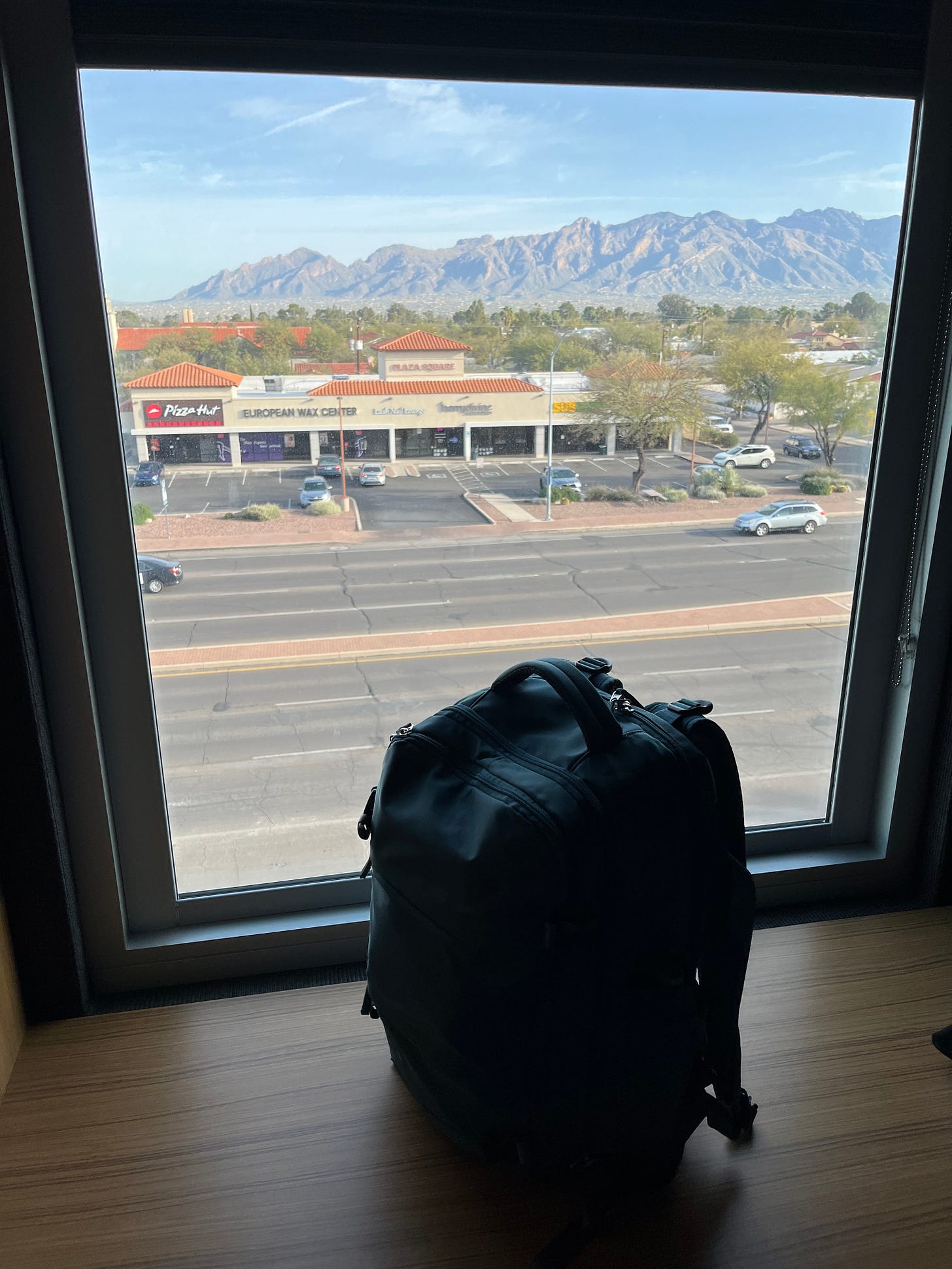 Picture of the view outside my hotel window, showing the Catalina mountains, a strip mall, and my single backpack propped up in front of it Picture of the view outside my hotel window, showing the Catalina mountains, a strip mall, and my single backpack propped up in front of it