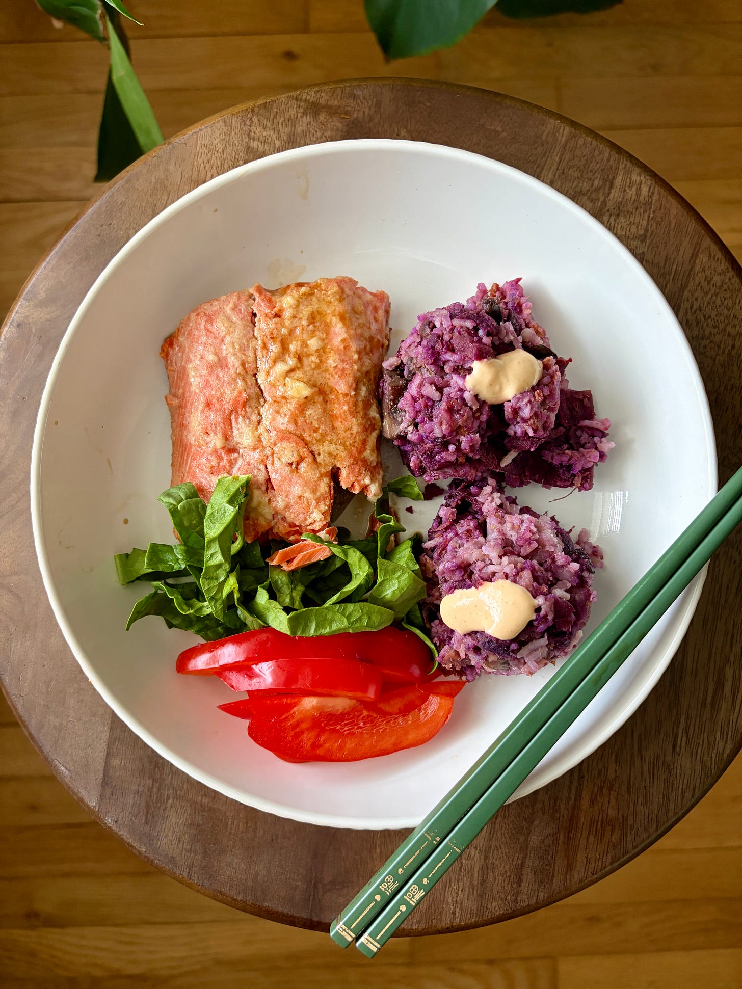 A nourishing honey miso salmon bowl with purple sweet potato mushroom rice, fresh sliced red bell pepper, and spinach, served with yum yum sauce.