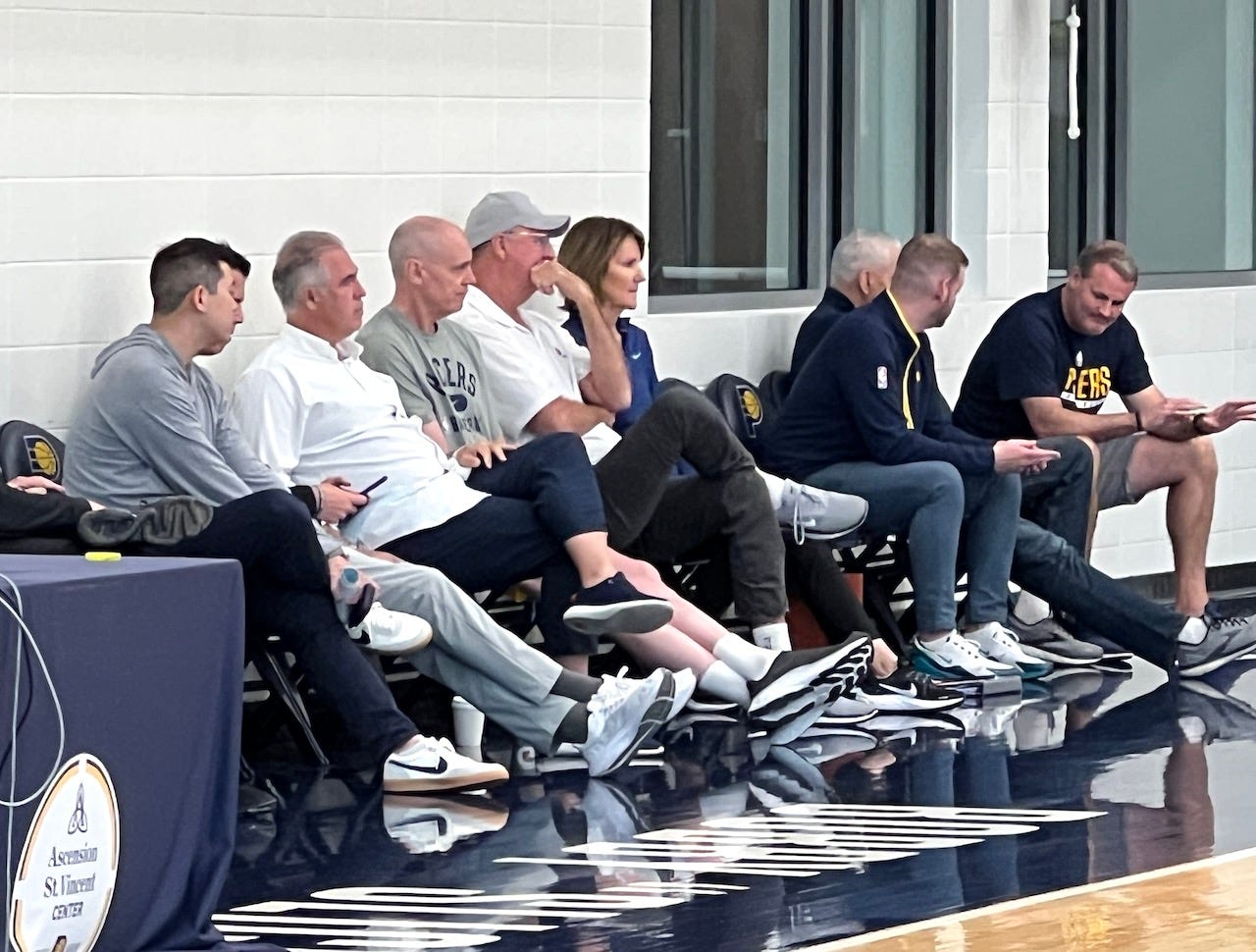 Larry Bird, wearing glasses and a hat, sits between head coach Rick Carlisle and assistant GM Kelly Krauskopf at a Pacers pre-draft workout.
