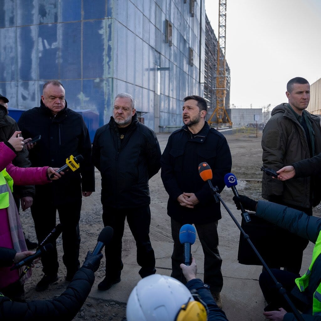 Volodymyr Zelensky, in a black coat, speaks to reporters.
