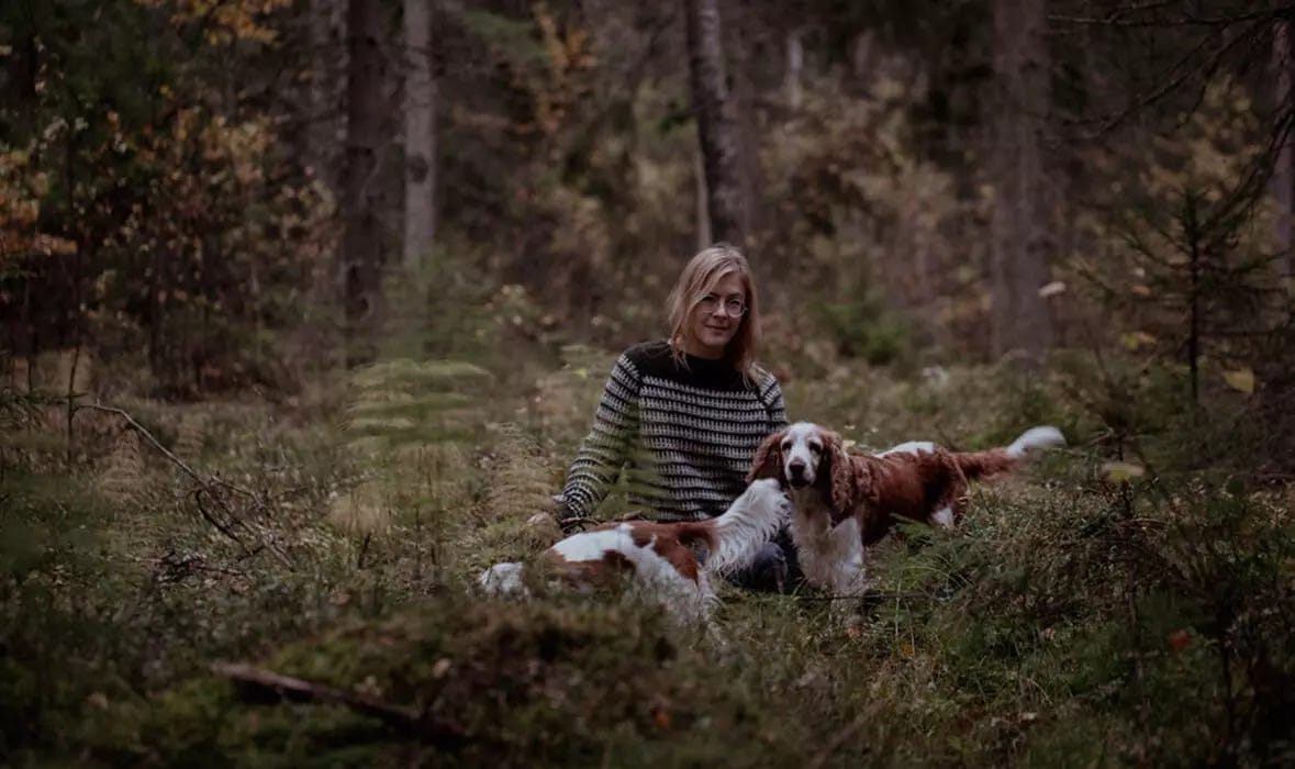 woman wearing a striped sweater sitting on a forest with 2 dogs