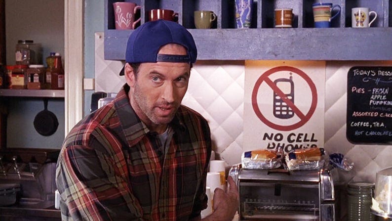 Luke Danes, a character from Gilmore Girls, points to a sign in his diner that reads "No Cell Phones"