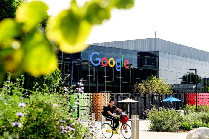 A man on a colorful bicycle riding past the Google headquarters building.