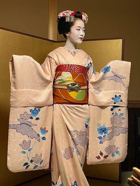 A collage of nine photos from travels in Japan: two sumo wrestlers posing with visitors; vintage kabuki posters on display; a small group sitting on tatami mats during a cultural workshop; a mannequin dressed in a traditional kimono with floral patterns; three people smiling in front of a lantern-filled temple gate; a night market vendor grilling skewers and takoyaki; two friends taking a selfie in Shibuya among bright city signs; the waterfront skyline and Ferris wheel in Yokohama; and a narrow alleyway in Kyoto lined with glowing izakaya lanterns.