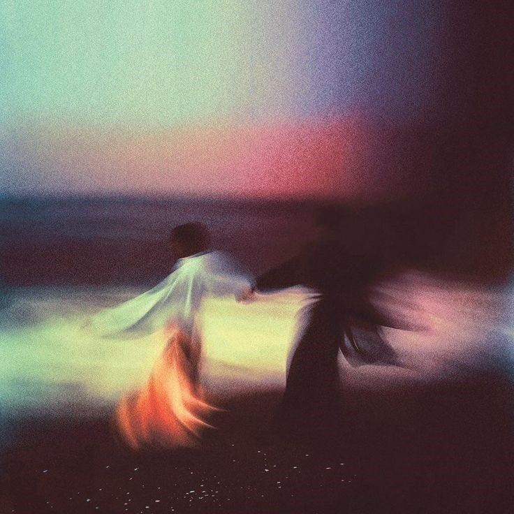 This may contain: blurry photograph of two people walking on the beach at night with colorful lights in the background