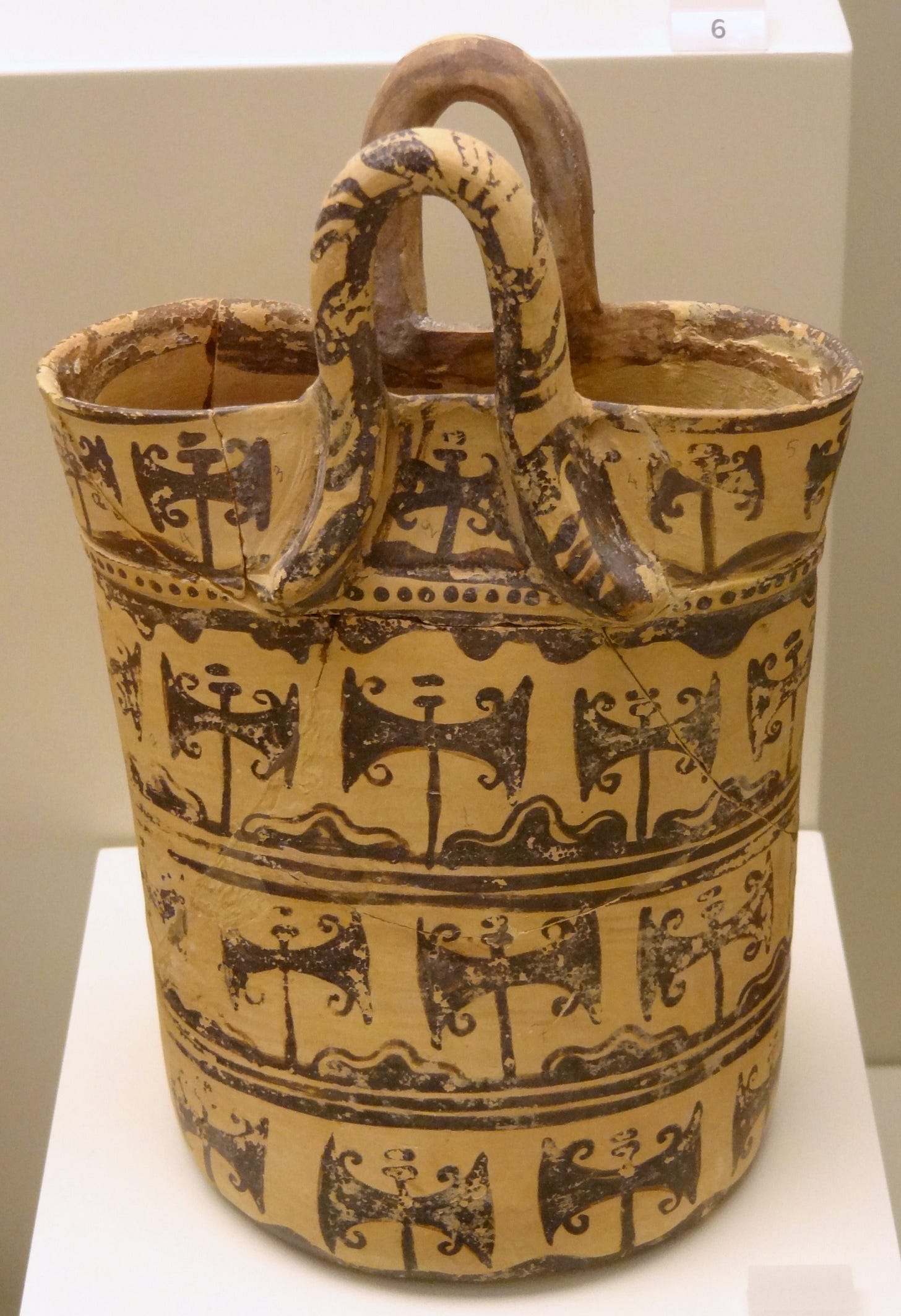 Cream-colored ceramic vessel with tall looped handles and black painted design of horizontal rows of vegetative labryses growing up from furrows between lumpy, rocky bits of earth.