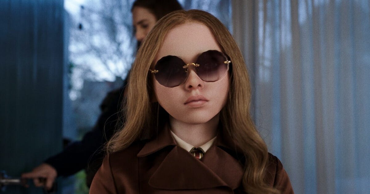 M3GAN wearing oversized round sunglasses and a trench coat, standing with an emotionless expression. M3GAN wearing oversized round sunglasses and a trench coat, standing with an emotionless expression.