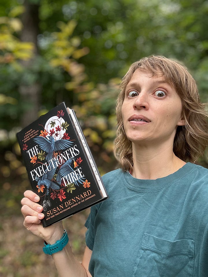Four photos of Sooz with The Executioners Three in front of the first autumn leaves of the season. In the first photo, she's smiling, in the second she's looking goofily afraid, in the third she's showing the printed edges that read Take Heed, and in the fourth, she's showing the gorgeous end papers that show the full color map