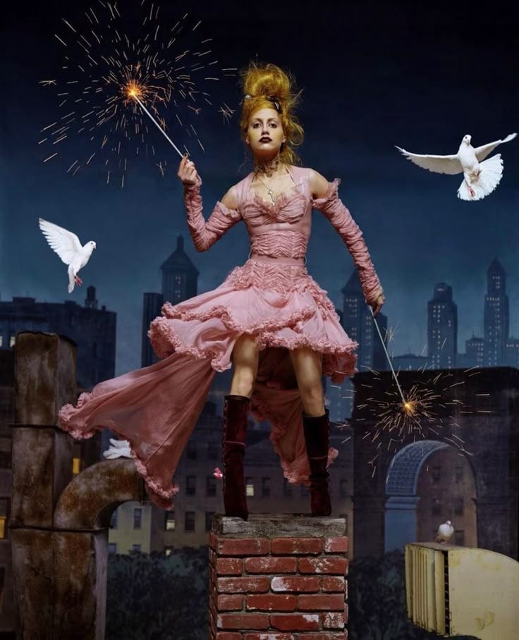 This may contain: a woman in pink dress standing on top of a brick wall holding a sparkler