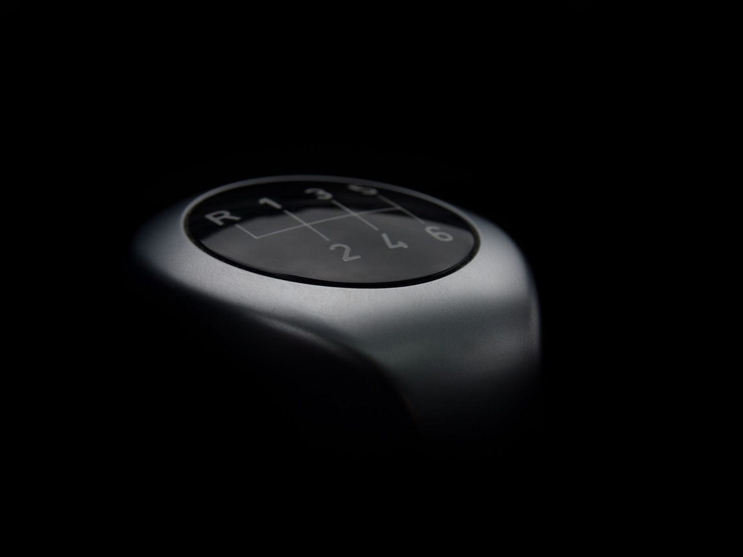 A gray stickshift with reverse and first through sixth gears diagrammed on top of an all-black background. A gray stickshift with reverse and first through sixth gears diagrammed on top of an all-black background.