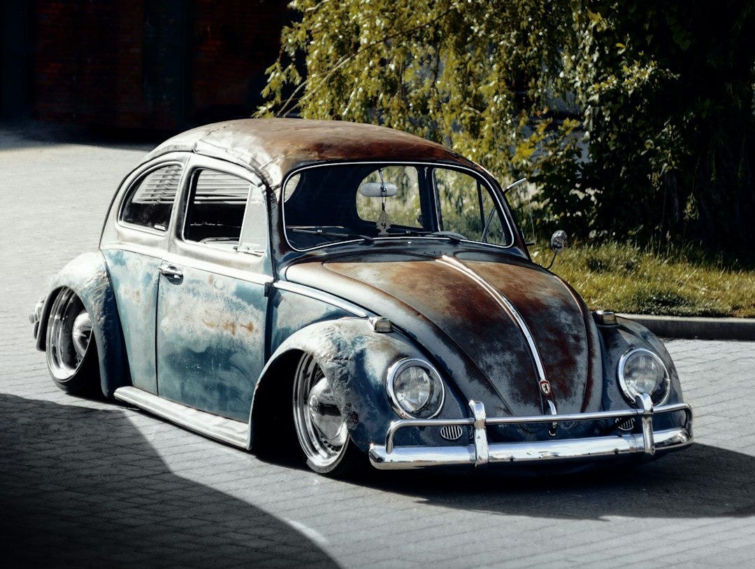 a rusted volkswagen beetle sitting on the side of a road