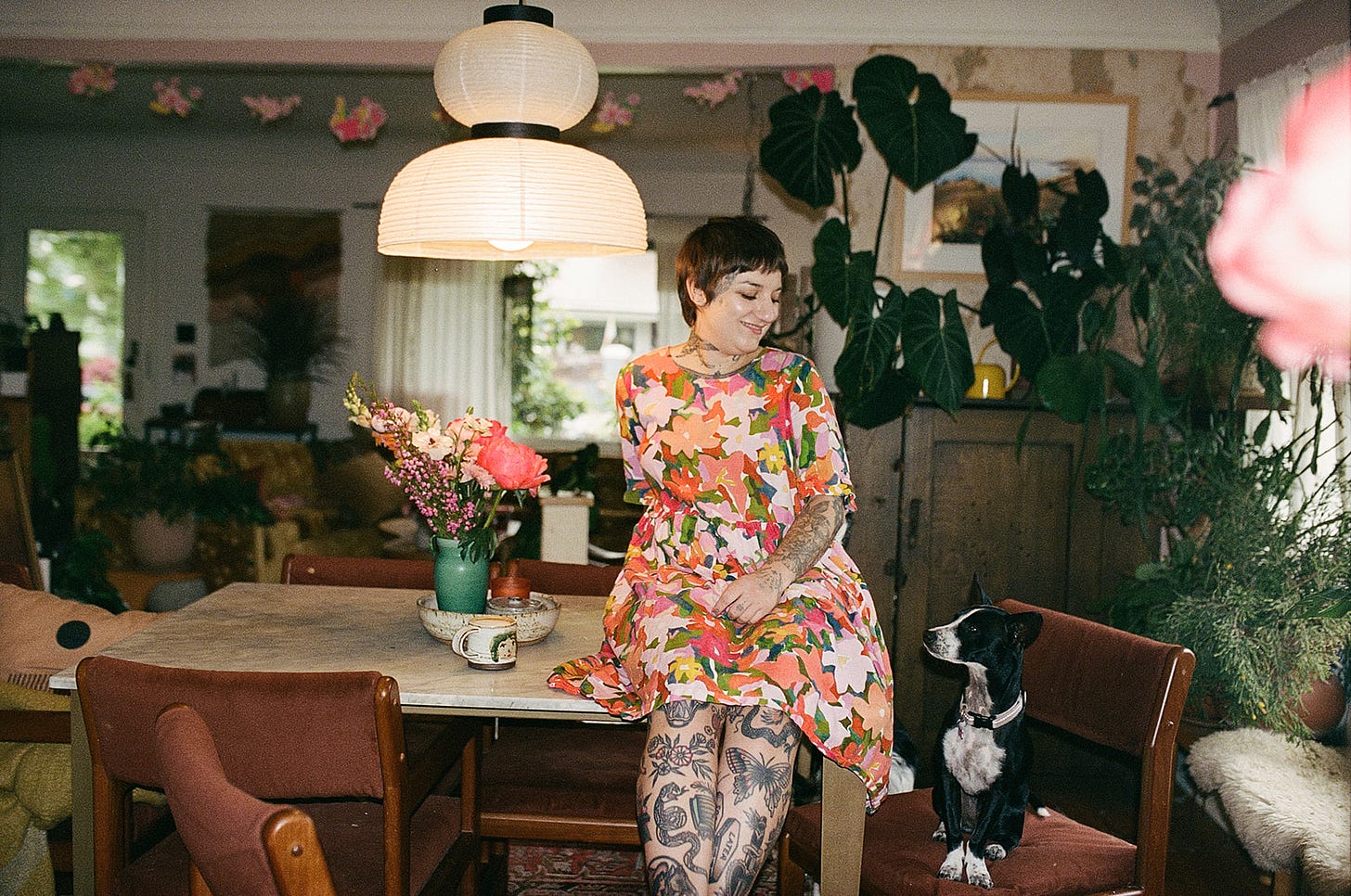 woman sits on marble table looking at small black and white dog who sits on a chair below her