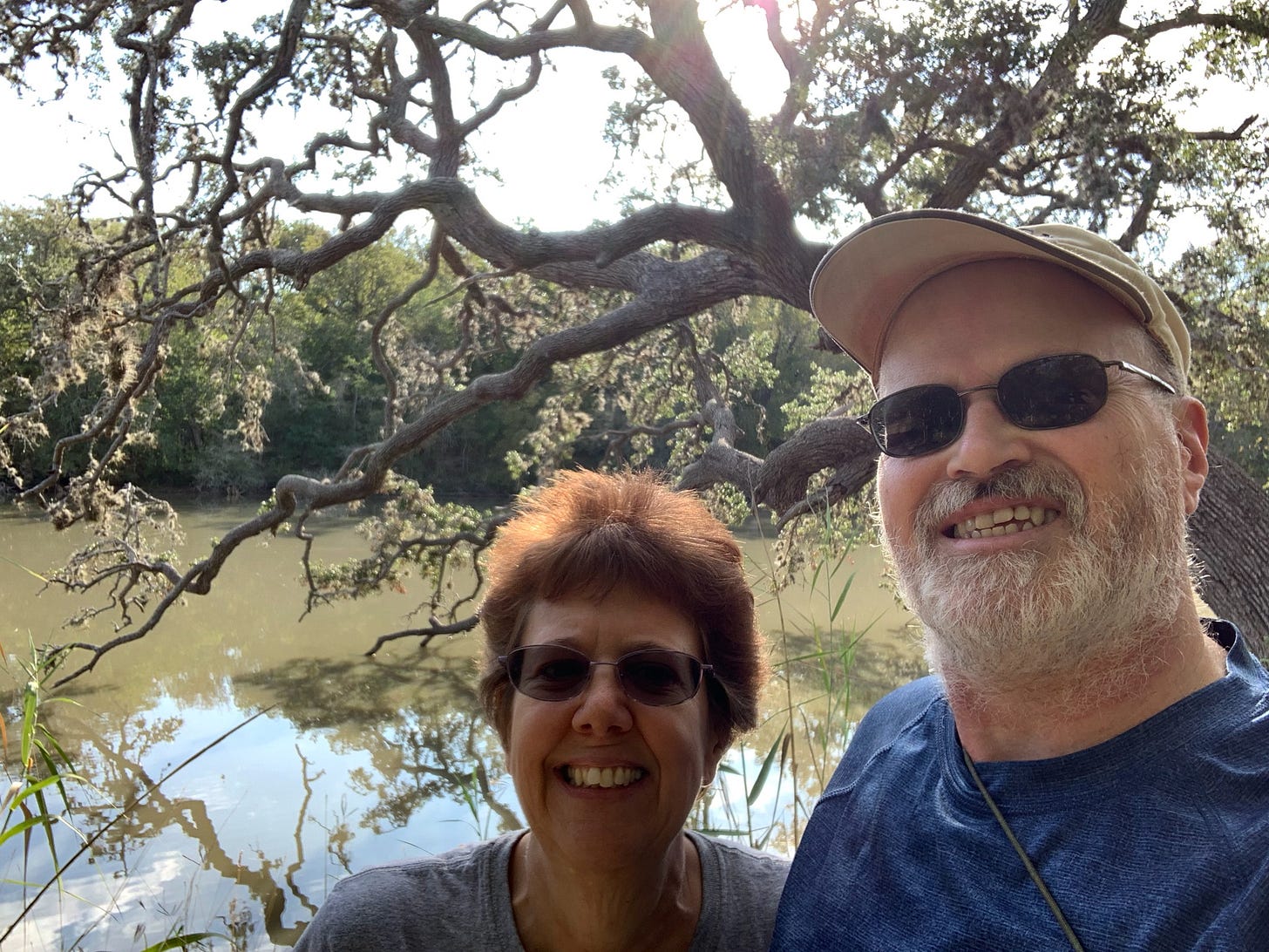 Author Wendi Gordon with her husband Steve standing in front of a tree with branches extending over a lake