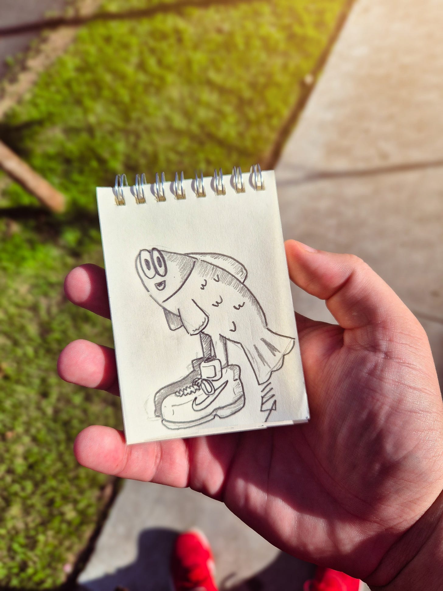 Foto de uma mão segurando um bloco de notas. No bloco, o desenho de um peixe usando sapatos da marca Nike