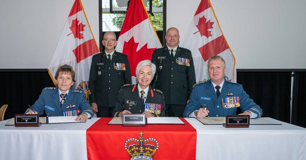Three people in military uniform, signing a document. Two people in military uniform stand behind.