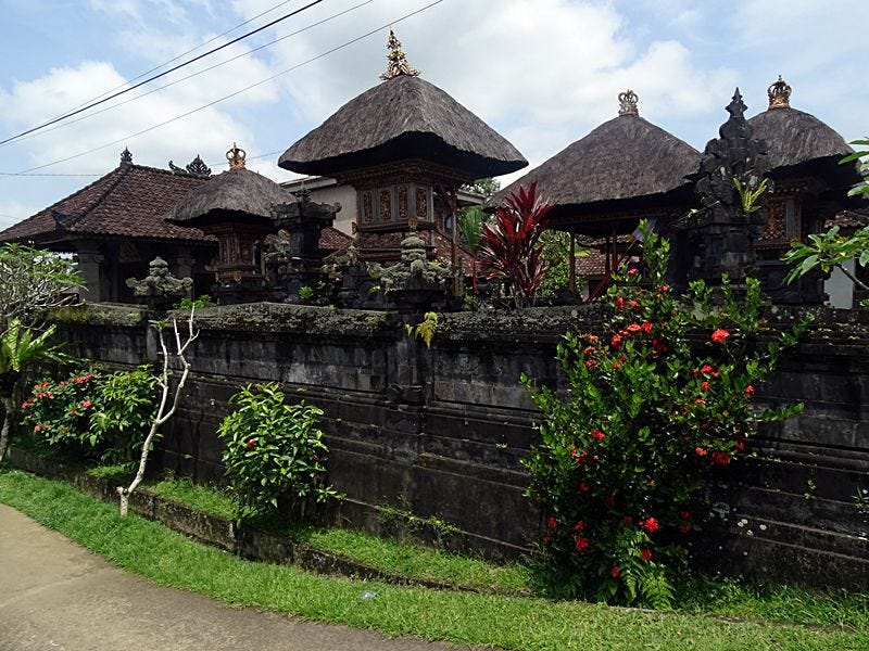 Traditional Balinese family compound in Delod Sema village, Bali, with stone walls, temple-style gateways, and lush tropical plants.
