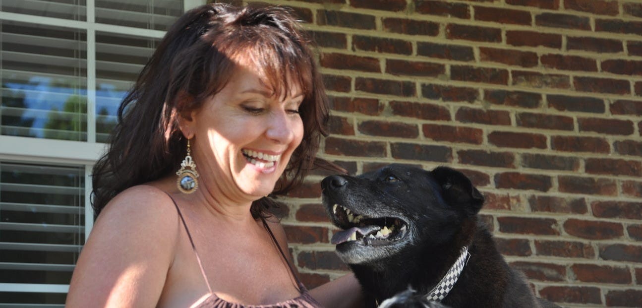 Author smiling with dappled sunlight on her face. Raki looking right into her face with eyes full of love. Raki is a black Lab/Chow mix. Author smiling with dappled sunlight on her face. Raki looking right into her face with eyes full of love. Raki is a black Lab/Chow mix.