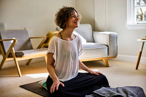 Dr Vicki Connop seated on a yoga mat beside photographs of the lush Waitākere Ranges and a towering native tree fern in West Auckland.